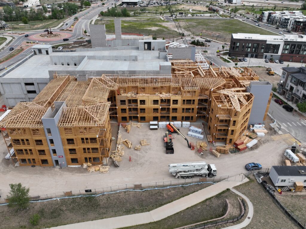 Drone aerial of a multi-family apartment building under construction with completed wood framing and concrete parking structure