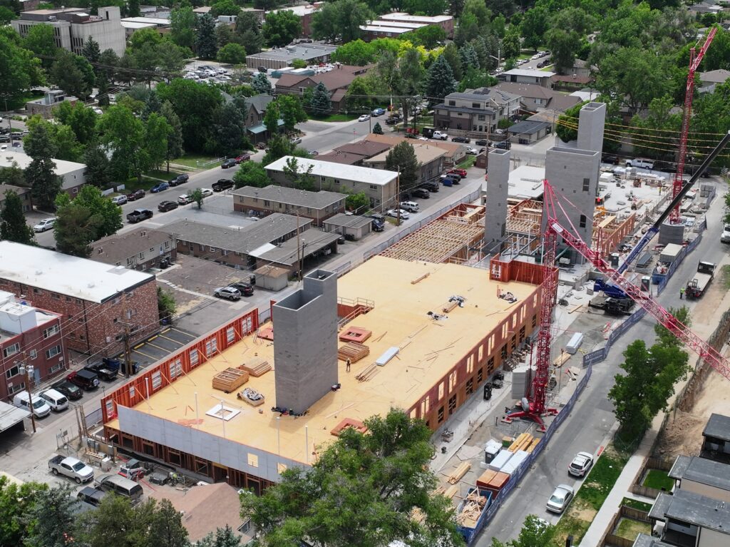 Drone oblique view of a multi-story residential construction project with wood framing, concrete cores, and tower cranes in an urban neighborhood