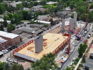 Drone oblique view of a multi-story residential construction project with wood framing, concrete cores, and tower cranes in an urban neighborhood