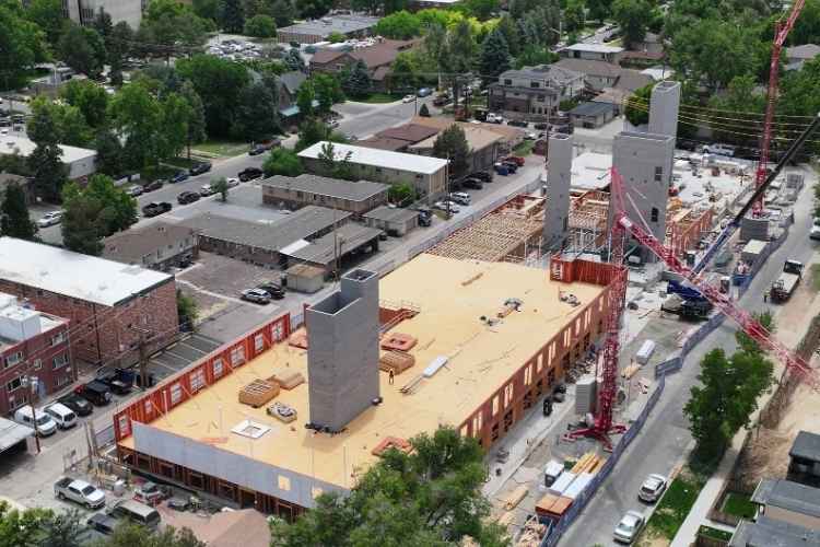 Drone oblique view of a multi-story residential construction project with wood framing, concrete cores, and tower cranes in an urban neighborhood