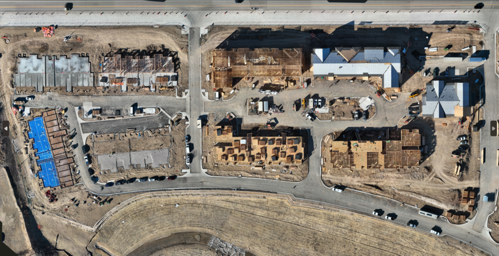 High-resolution drone aerial documenting construction progress across a multi-family residential development with framing, roofing, and site infrastructure in Arvada, Colorado